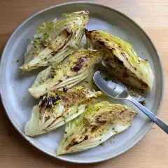 Grillad spetskål med citron och örter på en ljusgrå tallrik. En sked ligger på tallriken.