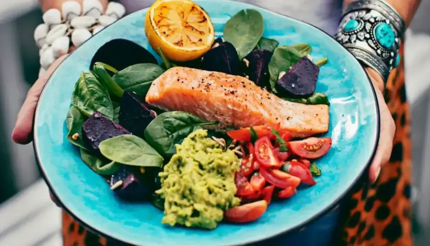 En matig sallad med lax, avokado, rödbetor, tomater och citron på en turkos tallrik.