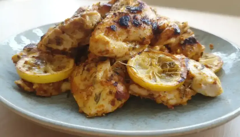 En tallrik med saftig, grillad kallskuren kyckling med citronskivor. Kryddorna ger kycklingen en härlig färg.
