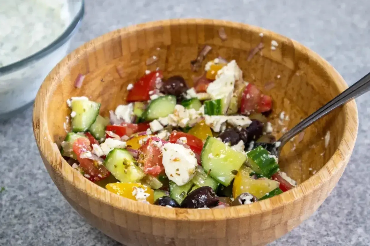 En härlig grekisk sallad med tomater, gurka, oliver och fetaost i en träskål.