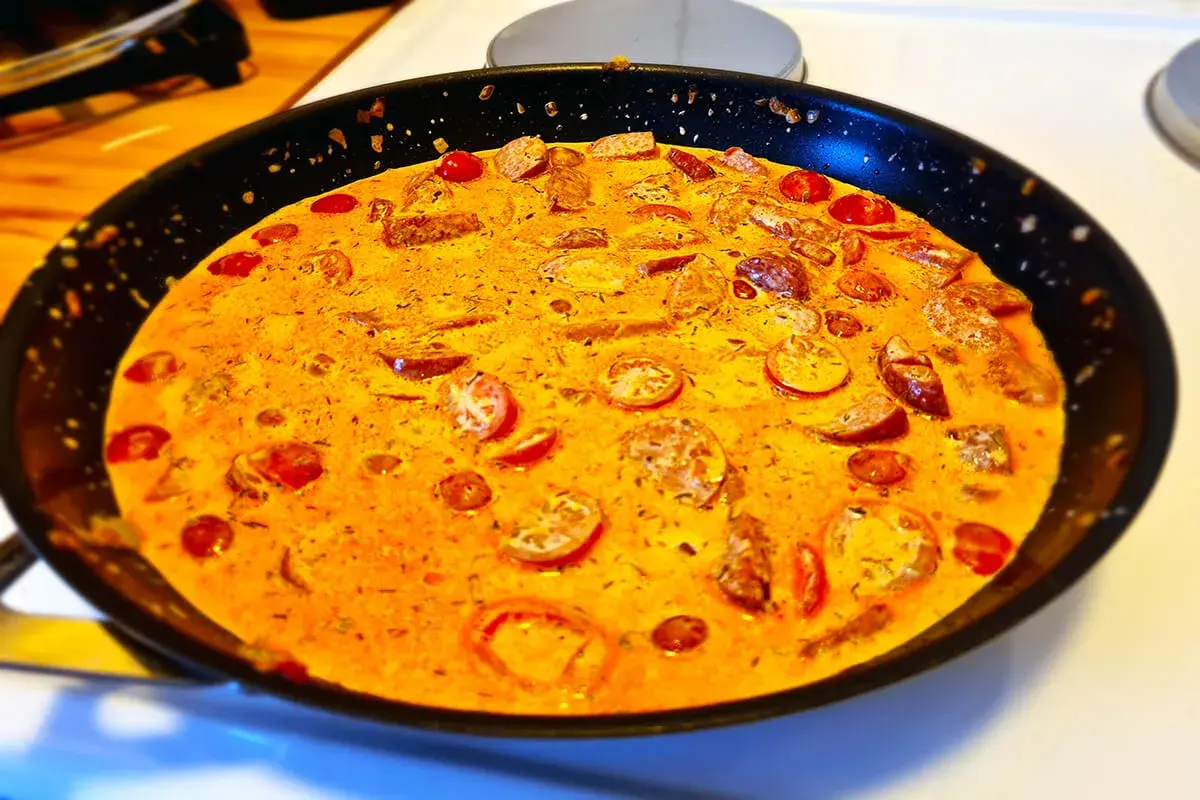 En krämig korv stroganoff deluxe i en stekpanna, med skivad korv och körsbärstomater i en gyllene sås.