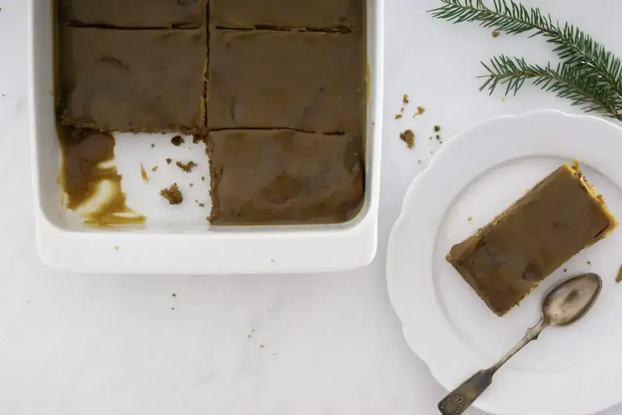 En bit av en härlig sticky toffee pudding i en vit form, en annan bit ligger på en tallrik med en sked.
