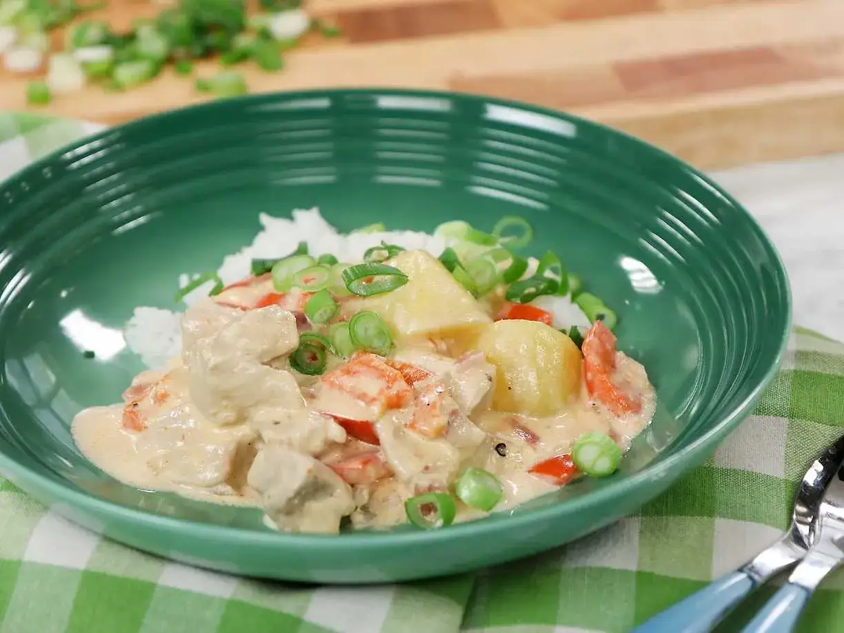 En krämig kycklinggryta med ris, toppad med färsk salladslök och bitar av ananas. En härlig kycklinggryta med ris som ser utsökt ut.