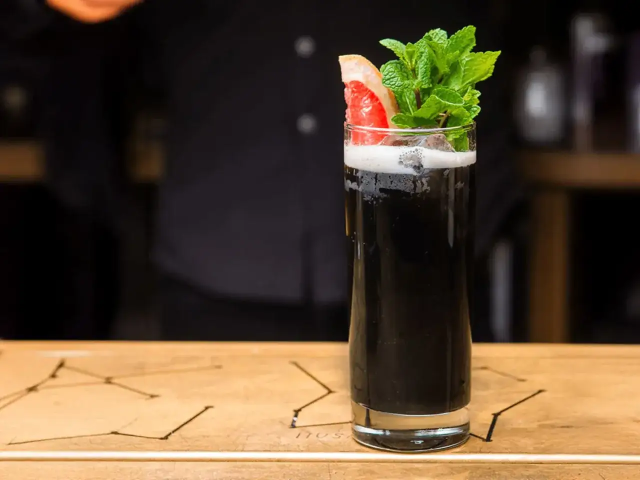 En hög, elegant glas med en mörk, svart drink. Garnerad med en grapefruktklyfta och färsk mynta.