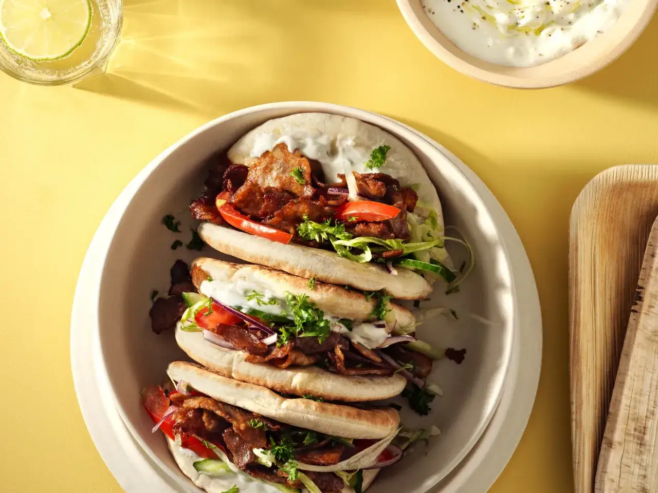 Tre gyros kebab-rullar fyllda med kött, grönsaker och sås. En glas med limevatten och en skål med dippsås syns också.