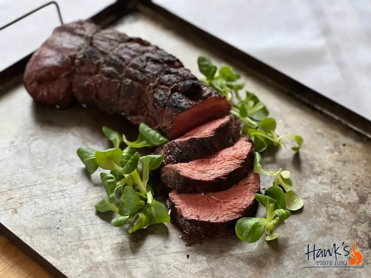 Perfekt grillad oxfil&eacute;, saftig och r&ouml;d inuti, serverad med f&auml;rska gr&ouml;na blad p&aring; en rustik bricka.