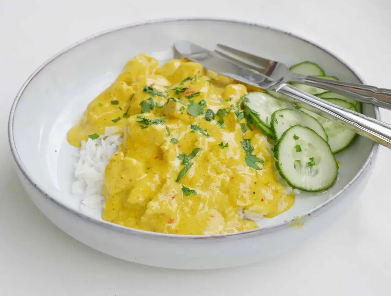 En kr&auml;mig kyckling curry gryta serveras med ris och gurkskivor. En h&auml;rlig och smakrik r&auml;tt.
