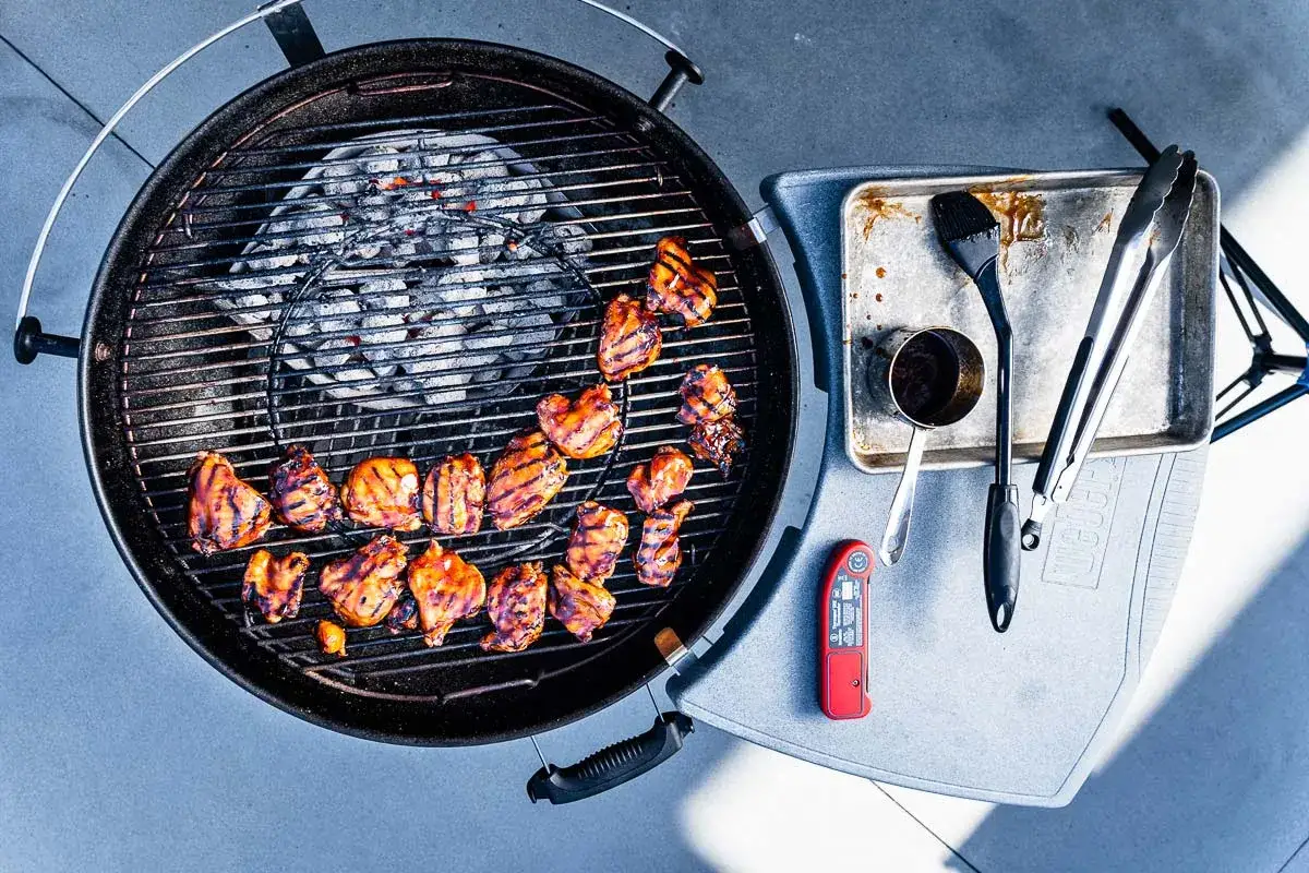 Grillad kyckling på en klotgrill bäst i test, med tillbehör som pensel, tång och termometer.