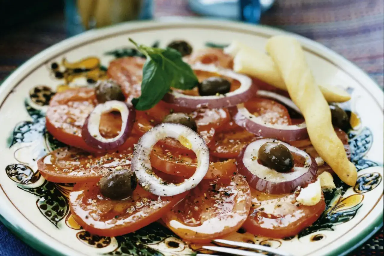 En läcker italiensk potatissallad med tomater, rödlök, oliver och basilika, serverad med grissini.