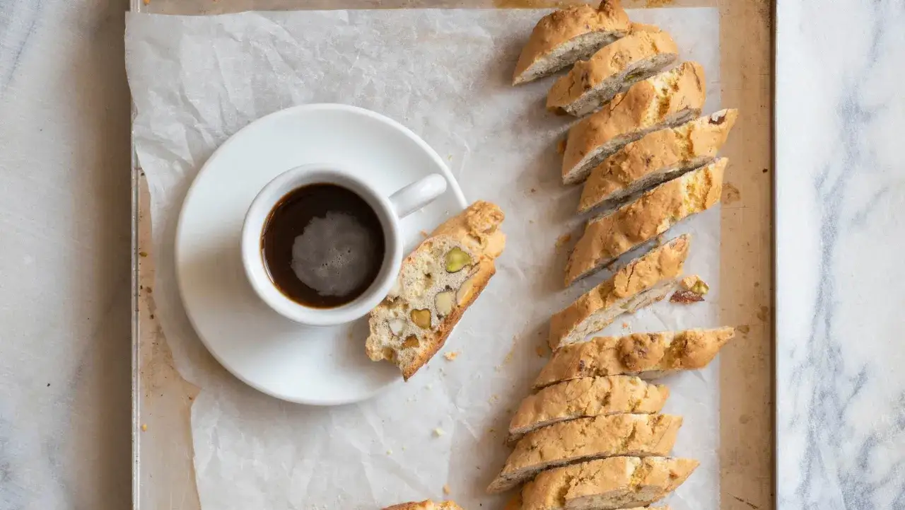 En kopp kaffe bredvid en rad italienska mandelskorpor med pistagen&ouml;tter och mandlar.