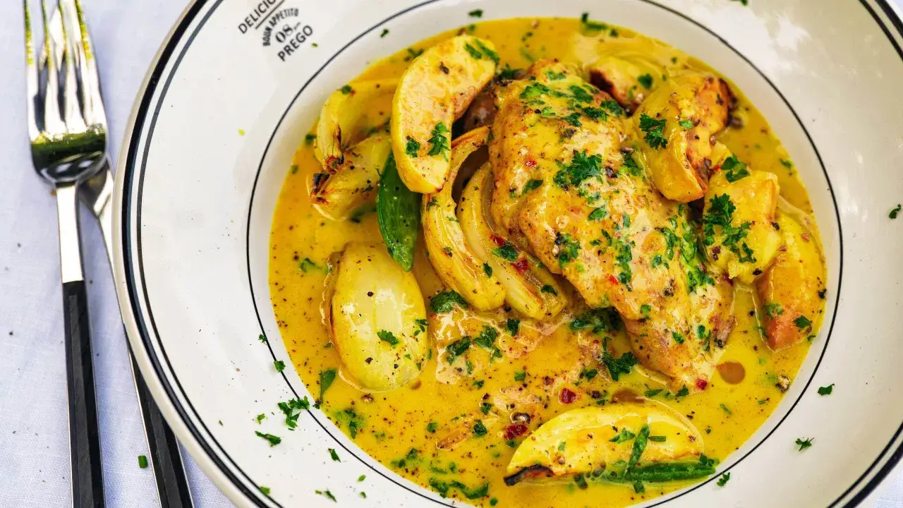 Kyckling i krämig, gul sås med grönsaker, liknande tikka masala, serverad på en tallrik med en gaffel bredvid.
