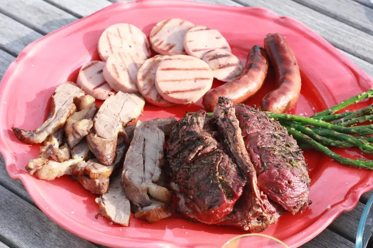 En stor röd bricka med grillad rådjur, korv, grillad korv och sparris. En härlig sommarmåltid!