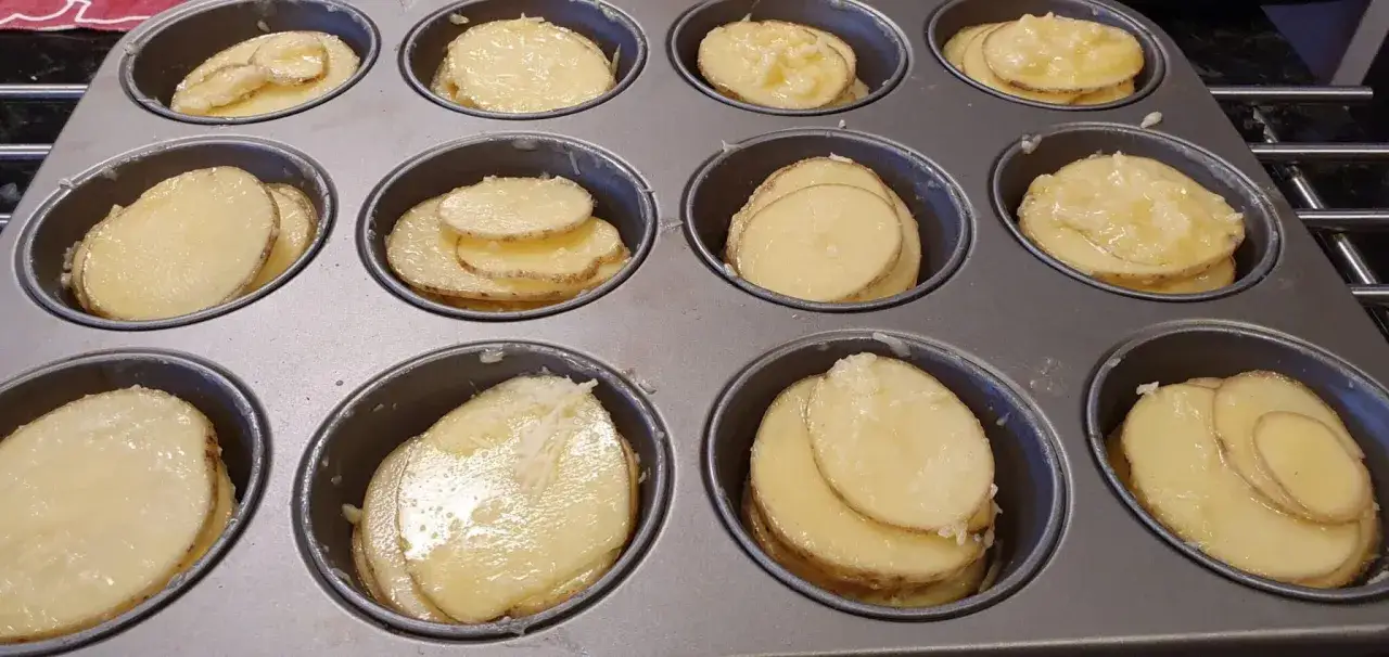 Tunna skivor av potatis i muffinsformar, redo att bakas. En härlig syn av potatis i muffinsform!