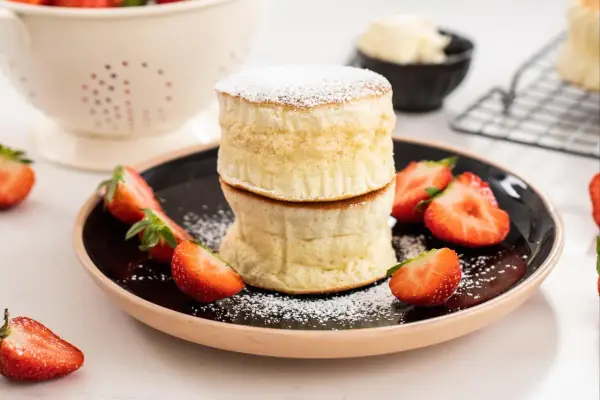 Två fluffiga japanska pannkakor staplade på en tallrik med färska jordgubbar och pudersocker.
